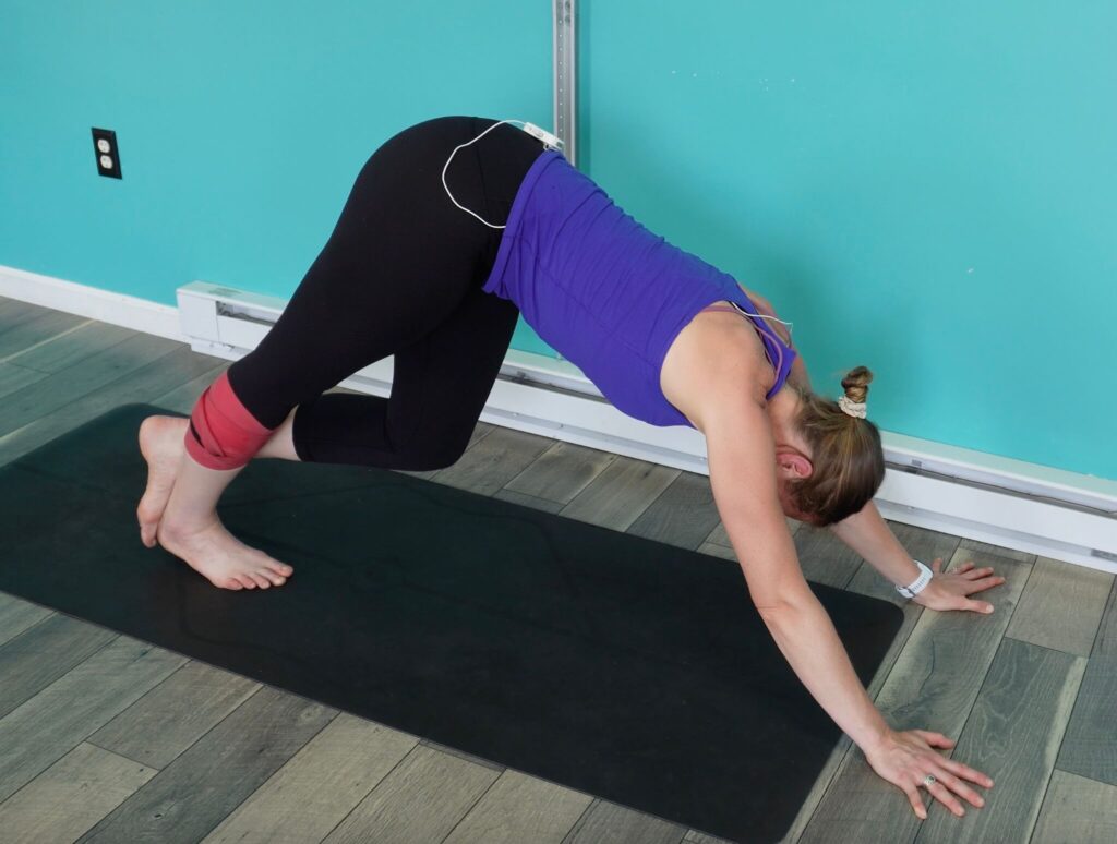 Dr. Chloe in an A frame position with her arms extended infront of her, her hips towards the ceiling, and her weight shifted over to the calf that is wrapped in a muscle floss band.